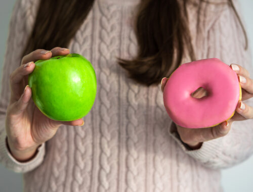 Young woman holding a doughnut and green apple in her hands. Concept of healthy and unhealthy food, clean eating, lifestyle, dieting, and fitness